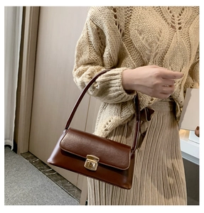 Détail du sac sous l'aisselle en cuir marron foncé avec boucle dorée porté à l'épaule