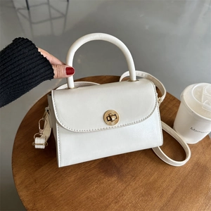 Vintage white square crossbody bag with gold metal lock on a wooden table with coffee