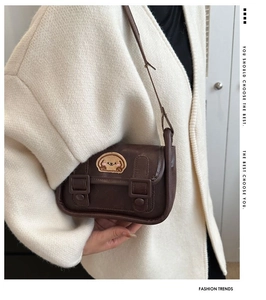 Gros plan du sac bandoulière marron vintage avec écusson chien sur un cardigan en maille