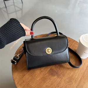 Mini black square handbag with golden twist lock and top handle on a wooden table