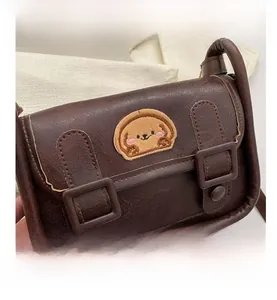 Détail d'un sac bandoulière marron avec broderie chiot mignonne et boucles décoratives