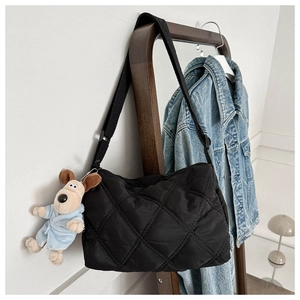 Close-up of black quilted nylon crossbody bag with cute dog plush charm on a wooden rack
