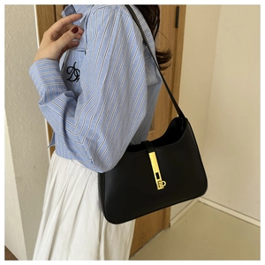 Détail d'un sac sous le bras en cuir noir avec un fermoir métallique doré minimaliste