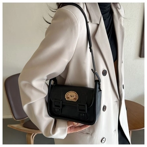 Détail d'un sac bandoulière en cuir noir avec un écusson animal de dessin animé marron