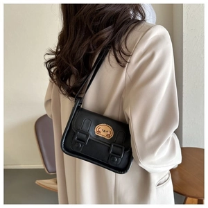 Détail d'un sac bandoulière noir avec écusson chiot en peluche sur un blazer beige chic
