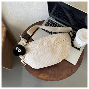 Detail of beige corduroy waist bag with plush soot sprite charm on wooden desk background