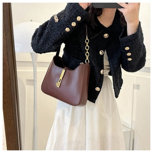 Detail view of dark brown leather baguette bag with a gold piston-style lock and chain strap