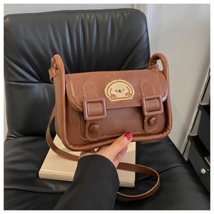 Détail d'un sac bandoulière en cuir marron avec écusson de chien et fermeture à boucle