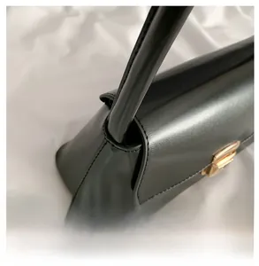 Gros plan du sac à bandoulière en cuir noir avec texture lisse et boucle en métal doré