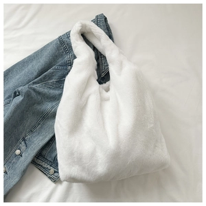 Detail der weichen weißen Kunstfell-Textur einer Hobo-Tasche auf Denim-Hintergrund