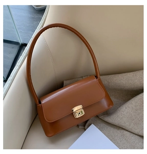 Détail du sac bandoulière en cuir marron avec fermoir métallique doré sur un canapé
