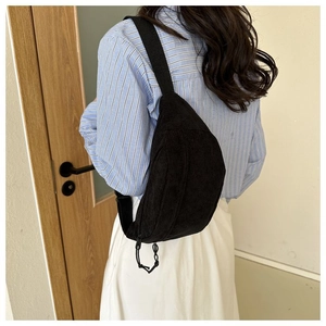 Close-up of black corduroy crescent chest bag worn with light blue striped shirt