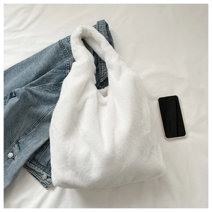 Draufsicht auf eine große weiße Kunstfell-Einkaufstasche auf einem Bett mit Jeansjacke