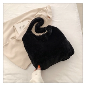 Close-up of black fluffy plush shoulder bag on a white bed with aesthetic background decor