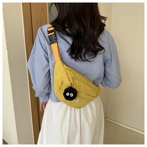 Detail of yellow corduroy crossbody bag featuring a soot sprite plush charm and strap
