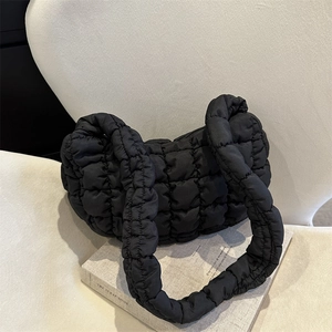 Chic black quilted cloud bag with puffy texture on a vintage book over a white chair