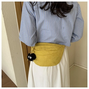Detail of yellow corduroy belt bag featuring a plush black spirit charm and zip closure