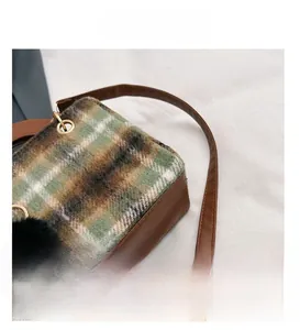 Close-up of vintage green plaid wool shoulder bag with leather trim and pompom detail