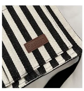 Détail du cabas en toile rayée montrant la texture tissée et l'étiquette mode en cuir brun