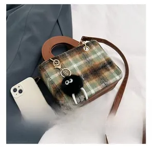 Detail presentation of small tweed crossbody bag next to phone for size comparison