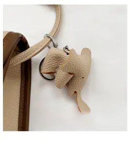Detail of beige litchi grain leather elephant charm with silver hardware on wide strap