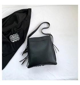 Detail shot of black leather tote bag with stylish fringe tassels on a white fabric background
