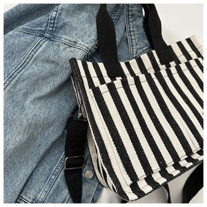 Détail d'un sac cabas en toile rayée avec bandoulière réglable et attaches en métal