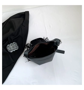 Close-up of black bucket bag featuring side fringe tassels and adjustable shoulder strap