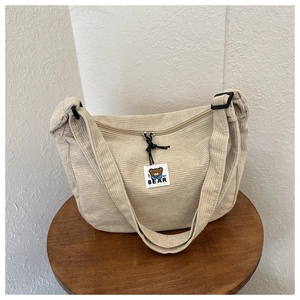 Detail of beige corduroy crescent bag showing fabric texture and MF BEAR logo patch
