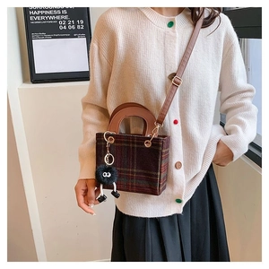 Detail of wool plaid handbag with leather handle and plush charm on a model