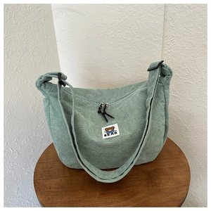 Detail of light green corduroy messenger bag featuring a bear logo on a wooden stool