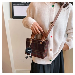 Detail of brown plaid wool crossbody bag with a plush charm on a beige knit cardigan
