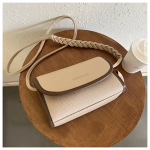 Detail of beige lychee leather crossbody bag with brown edges and woven strap design