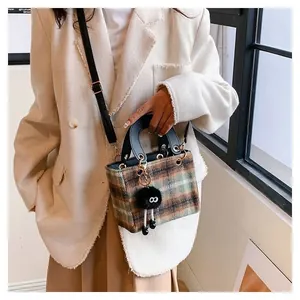 Detailed view of plaid wool handbag featuring a black fur ball charm and leather handle