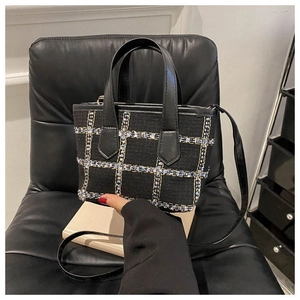 Dettaglio della borsa tote in tweed nero a scacchi posata su un libro bianco decorativo
