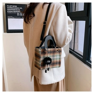 Detail of vintage plaid wool handbag with black leather handle and fur pompom charm