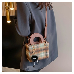 Detail of wool plaid crossbody bag featuring a plush monster charm and leather handle