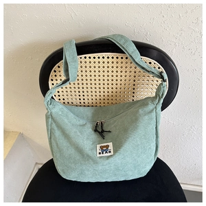 Detail of light green corduroy dumpling bag featuring cartoon bear patch on a chair