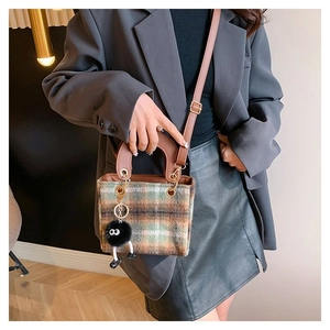 Detail of checkered woolen tote with brown leather straps and plush monster pendant