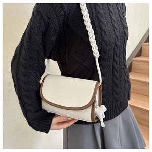 Detail of off-white lychee leather crossbody bag with brown piping and woven strap