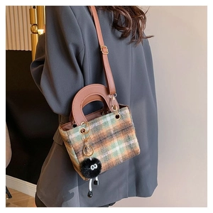 Detail of plaid wool crossbody bag with brown leather strap and fur eye charm detail