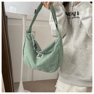Detail of green corduroy dumpling bag featuring adjustable strap and bear label
