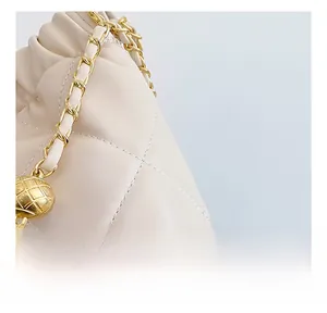 Detail of cream quilted leather texture with gold chain strap and metallic pineapple charm