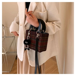Close-up of retro plaid wool handbag featuring black leather handles and plush charm