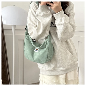 Green corduroy shoulder bag with bear patch shown worn by model in soft indoor lighting