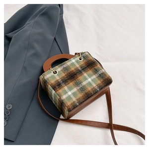 Detail of green plaid wool fabric and brown leather handle on a designer crossbody bag