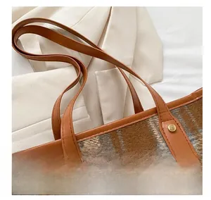 Detail of plaid wool fabric and leather handle with gold rivets on tote bag