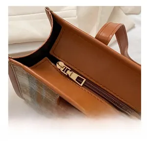 Detail of the smooth golden metal zipper and brown leather trim on a plaid tote bag