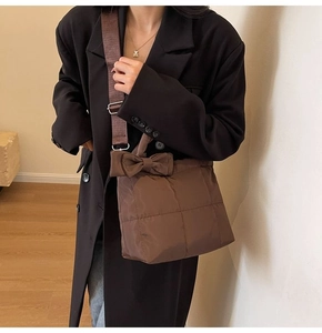 Gros plan du sac matelassé marron avec nœud décoratif et bandoulière large sur un blazer