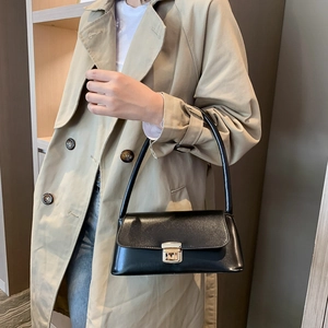 Sac sous le bras rectangulaire noir avec boucle dorée et cuir brillant porté par un modèle